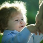 A little boy with long wavy hair touches his mother's face