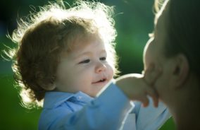 A little boy with long wavy hair touches his mother's face