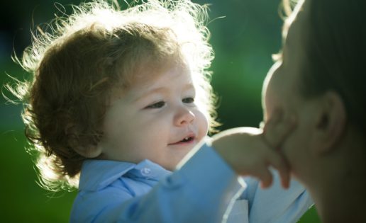 A little boy with long wavy hair touches his mother's face