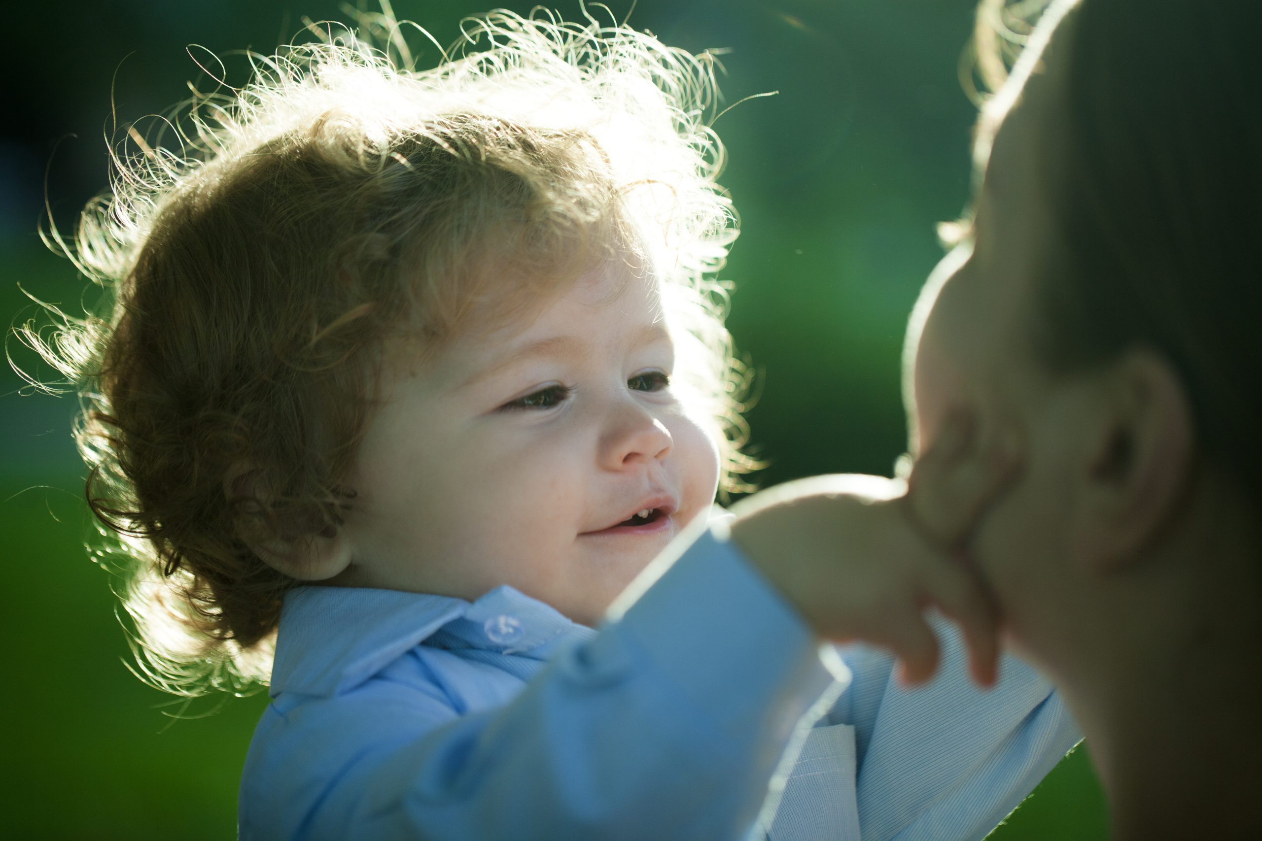 A little boy with long wavy hair touches his mother's face