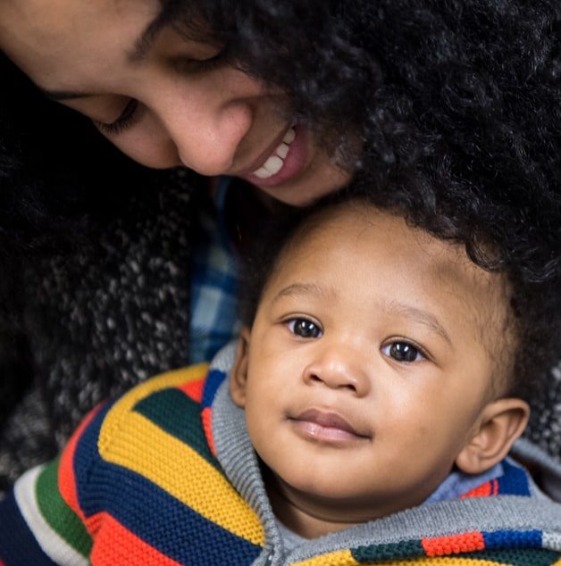 A mother is holding her son while looking down smiling at him as he is slightly smiling.