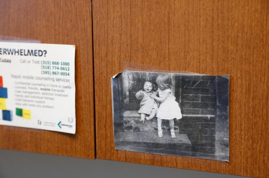 A closeup of an old image of two toddlers sitting on the steps of a home, that is taped to a cupboard in a doctors office.