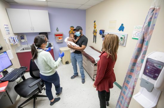 A female specialist is talking to a father who is holding his son in his arms while another female specialist is standing beside her.