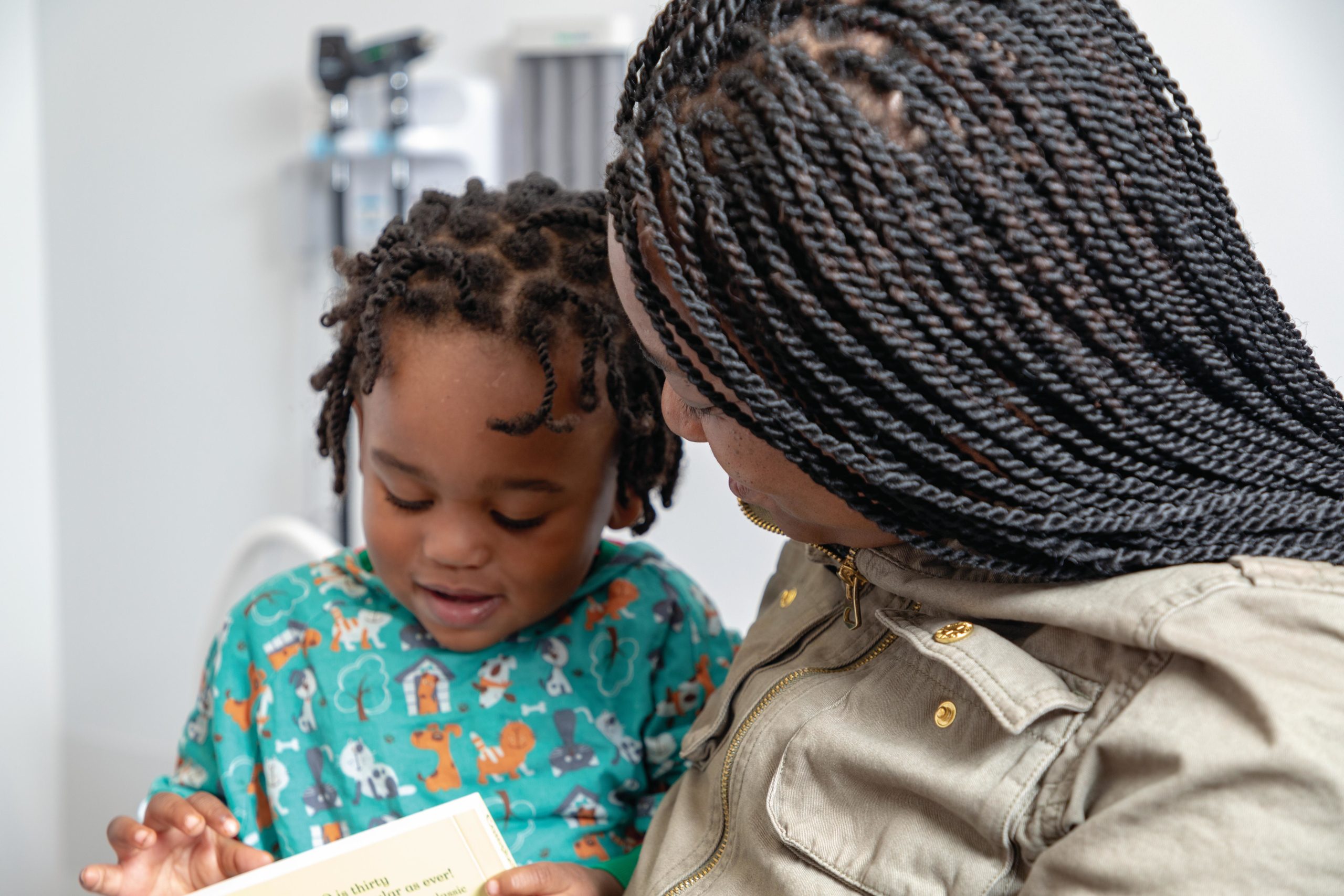 Toddler sits on mom's lap reading a book at the pediatrician's office